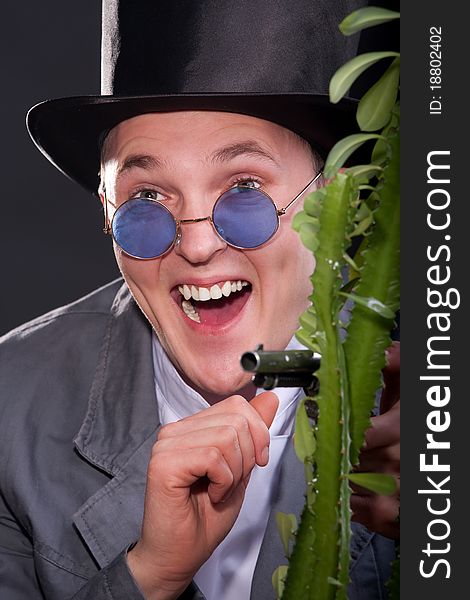 Emotional portrait of a man in a hat with a gun in his hand peek out from behind a plant