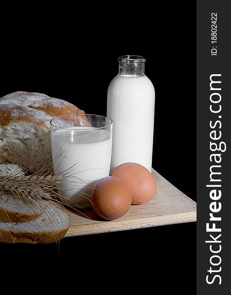 Bottle and cup of milk, eggs and bread on black