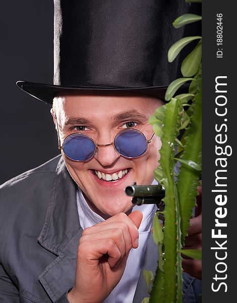 Emotional portrait of a man in a hat with a gun in his hand peek out from behind a plant