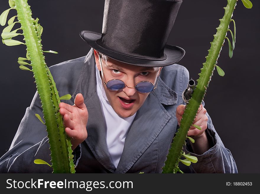 Emotional portrait of a man in a hat with a gun in his hand peek out from behind a plant