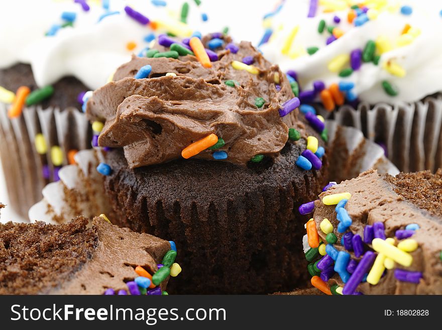 A macro image of chocolate cupcakes with festive sprinkles in sweet icing, wrap partially pulled back on one cupcake to display the delicious chocoate cake;. A macro image of chocolate cupcakes with festive sprinkles in sweet icing, wrap partially pulled back on one cupcake to display the delicious chocoate cake;