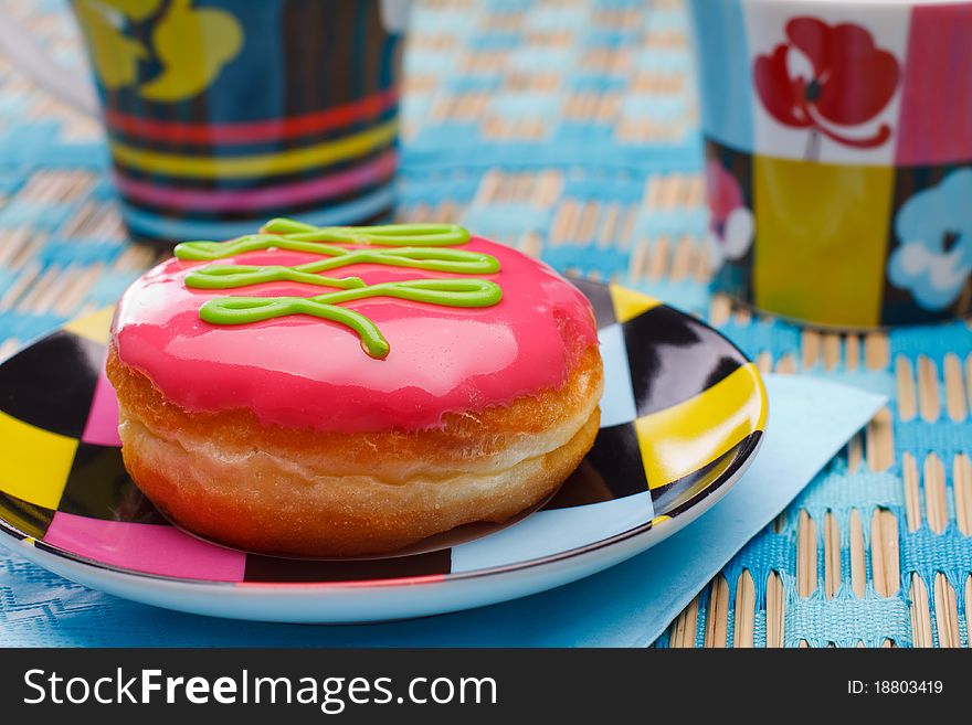 Tasty pink doughnut lying on a multicolored plate on a blue napkin. Tasty pink doughnut lying on a multicolored plate on a blue napkin