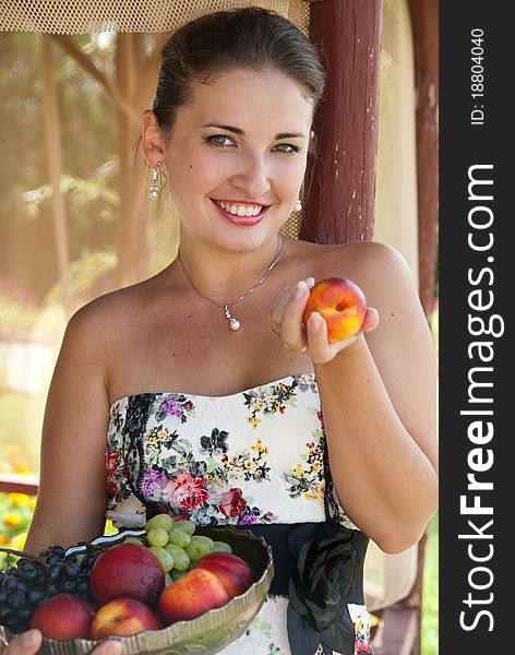 Beautiful brunette girl with fruits near the gazebo. Cheerful girl in a beautiful dress. Beautiful brunette girl with fruits near the gazebo. Cheerful girl in a beautiful dress.