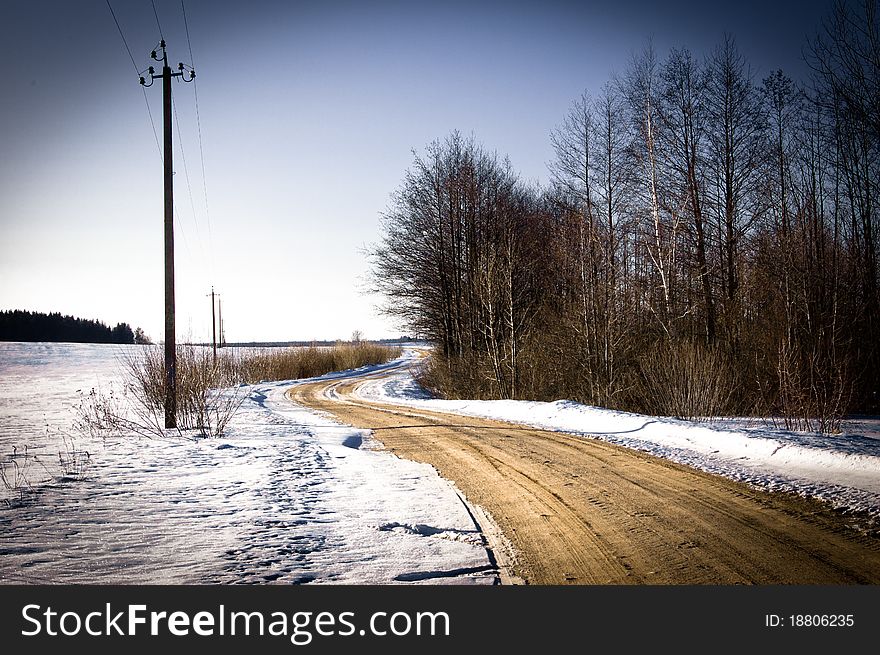 Landscape with the blue sky, road from gravel, snow, wood and bushes and a column. Landscape with the blue sky, road from gravel, snow, wood and bushes and a column