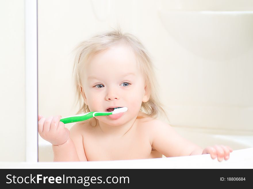 Adorable baby brushing teeth sitting in shower with dry hairs