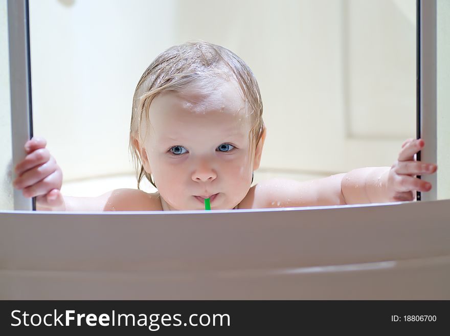 Adorable baby brushing teeth sitting in shower with light from top of shower