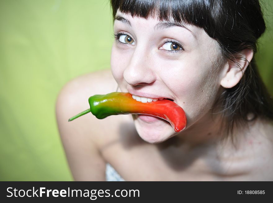 Happy young woman holding hot pepper in her teeth (mouth). Happy young woman holding hot pepper in her teeth (mouth)