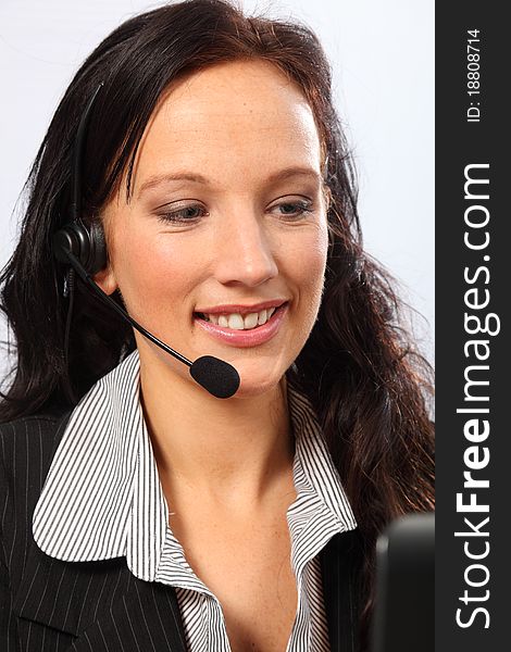 Beautiful young woman working in telesales with a smile, sitting to her computer speaking on a telephone headset. She is wearing a dark business suit. Beautiful young woman working in telesales with a smile, sitting to her computer speaking on a telephone headset. She is wearing a dark business suit.