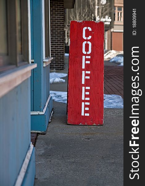 A red wooden sign sits on the sidewalk in front of a coffee shop. A red wooden sign sits on the sidewalk in front of a coffee shop