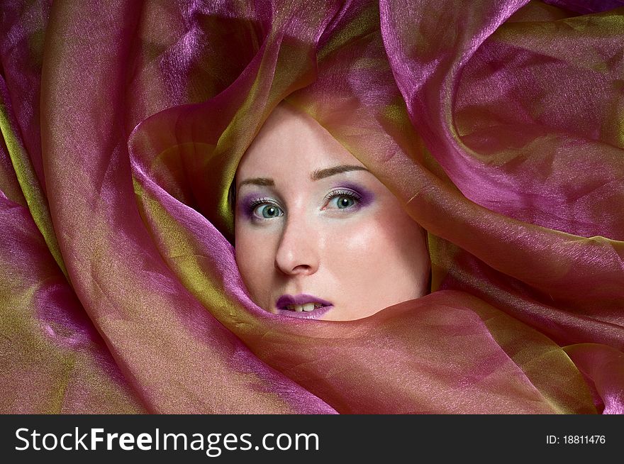 Woman's face with a bright make-up hiding in a fabric. Woman's face with a bright make-up hiding in a fabric.