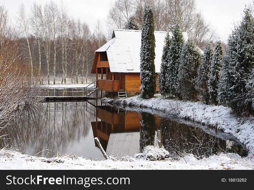 House on the lake. Early winter. Snow on the trees. House reflected on the water.