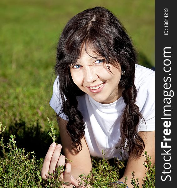 Portrait of beautiful brunette girl with blue eyes on green grass in the park.