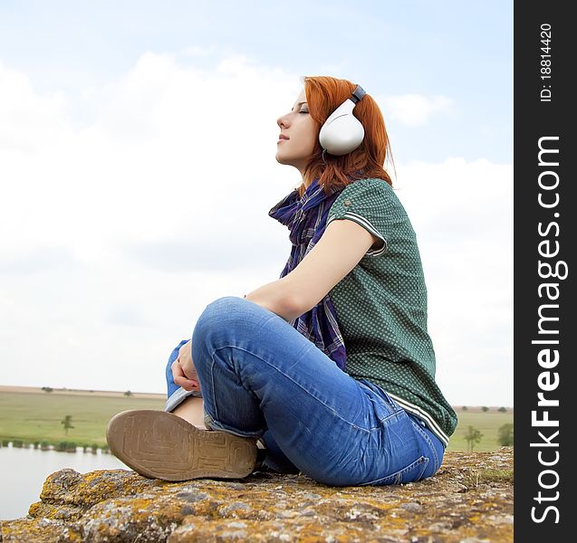 Girl with headphones at rock near lake.