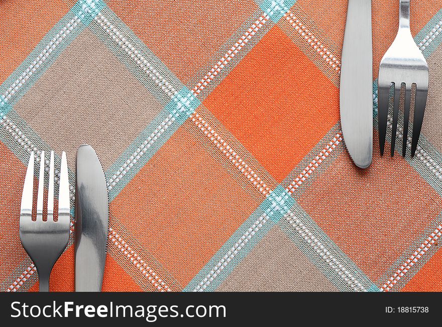 Two pair of forks and knives lying on chequered tablecloth