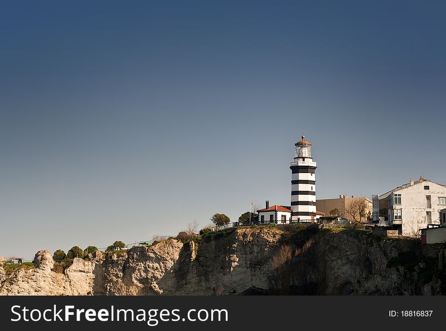 Landscape photo of a black and white striped lighthouse, near a cliff. Landscape photo of a black and white striped lighthouse, near a cliff.