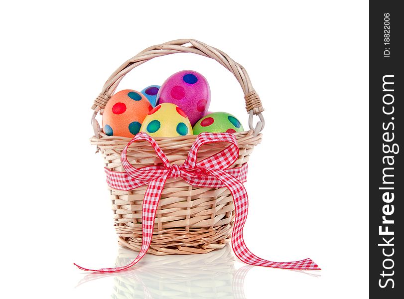 Colorful easter eggs painted with dots in a wicker basket with ribbon isolated over white