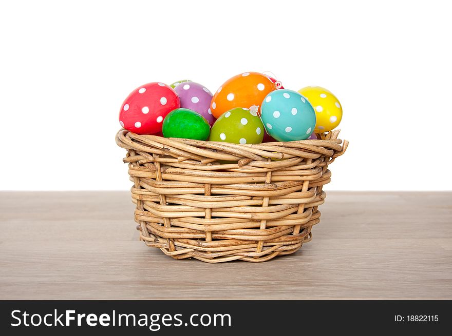 Colorful easter eggs painted with dots in a wicker basket on a table isolated over white