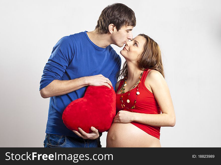 Man kissing his pregnant wife's nose holding red heart at hands. Man kissing his pregnant wife's nose holding red heart at hands