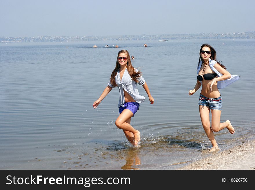 Happy young women running across the beach in shirts