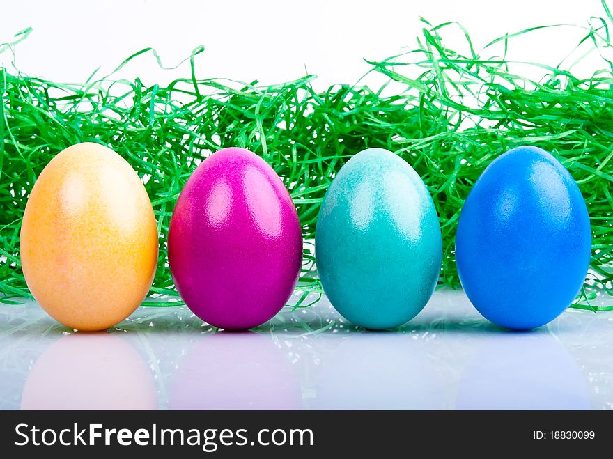 Four colored Easter eggs are on a white background with Easter grass. Four colored Easter eggs are on a white background with Easter grass