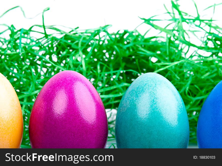 Four colored Easter eggs are on a white background with Easter grass. Four colored Easter eggs are on a white background with Easter grass