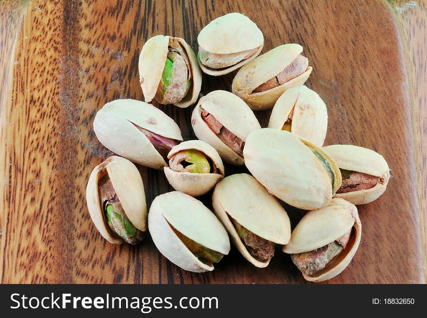 Pistachios roasted with salt lie in a wooden platter against a green background. Pistachios roasted with salt lie in a wooden platter against a green background