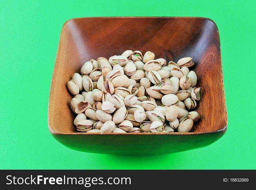 Pistachios roasted with salt lie in a wooden platter against a green background. Pistachios roasted with salt lie in a wooden platter against a green background