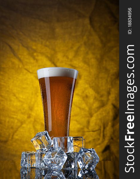 Beer in glass with ice cubes on yellow background