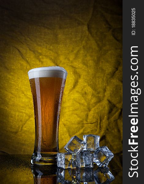 Beer in glass with ice cubes on yellow background