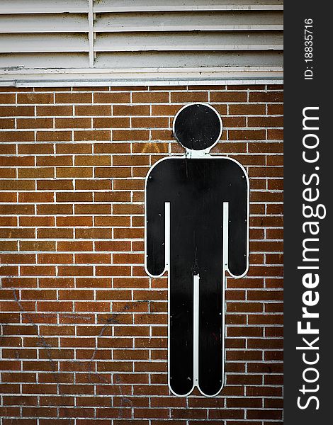 A human male AIGA international man symbol affixed to a red-brick wall. A human male AIGA international man symbol affixed to a red-brick wall