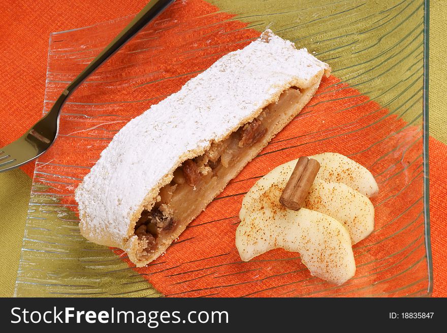 A slice of apple strudel served on a glass plate with apple slices and cinnamon. A slice of apple strudel served on a glass plate with apple slices and cinnamon