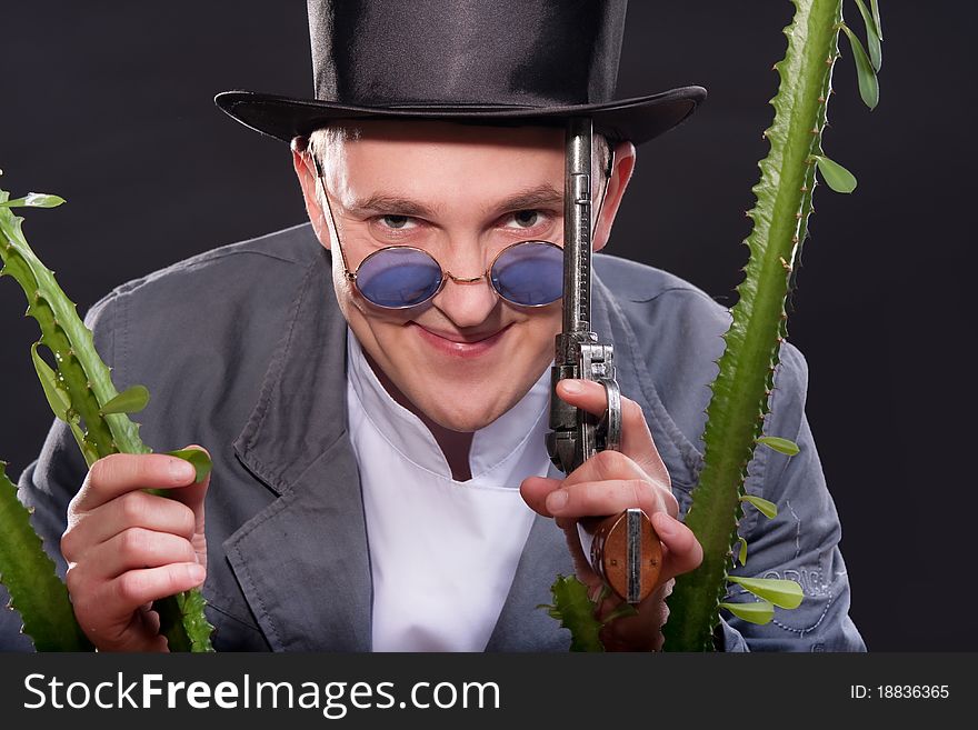 Emotional portrait of a man in a hat with a gun in his hand peek out from behind a plant