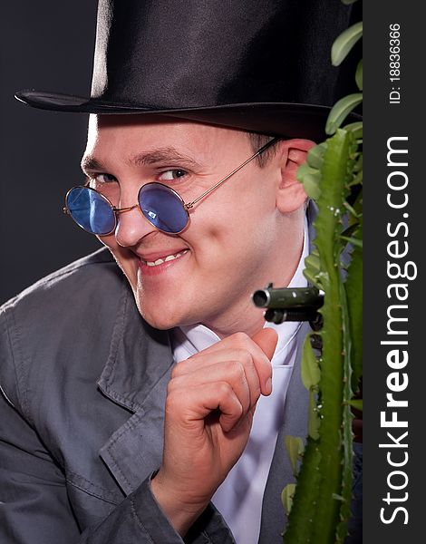 Emotional portrait of a man in a hat with a gun in his hand peek out from behind a plant