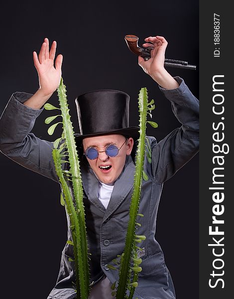 Emotional portrait of a man in a hat with a gun in his hand peek out from behind a plant