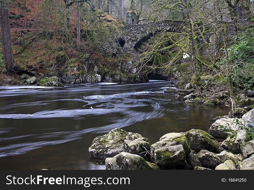 Stone bridge over waterfall in the highlands of scotland in winter with flowing water in foreground