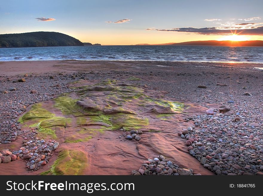 The sun sets in Five Islands, Nova Scotia, with some green algae lining the rocks in the foreground. The sun sets in Five Islands, Nova Scotia, with some green algae lining the rocks in the foreground.