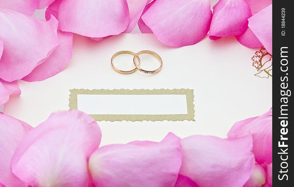 Wedding invitation in envelope with two rings, surrounded by rose leafs