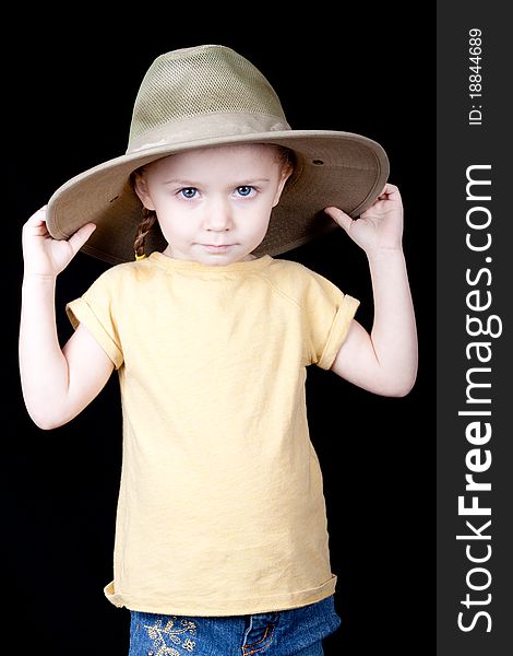 A young girl with a jungle style safari hat on. Her hands are on the hat and she is pulling it down. A young girl with a jungle style safari hat on. Her hands are on the hat and she is pulling it down.