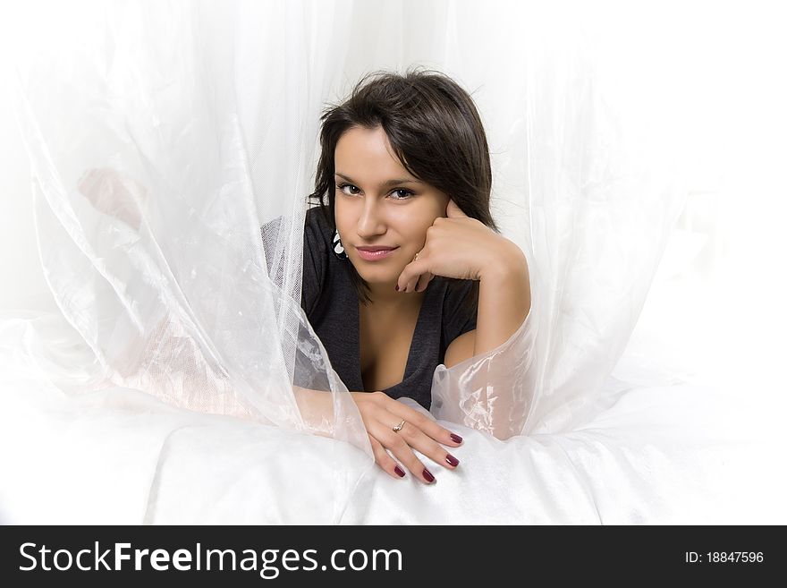 Close-up portrait of a young beautiful smiling girl with dark hair, bright nails and shining eyes, lying on the bed