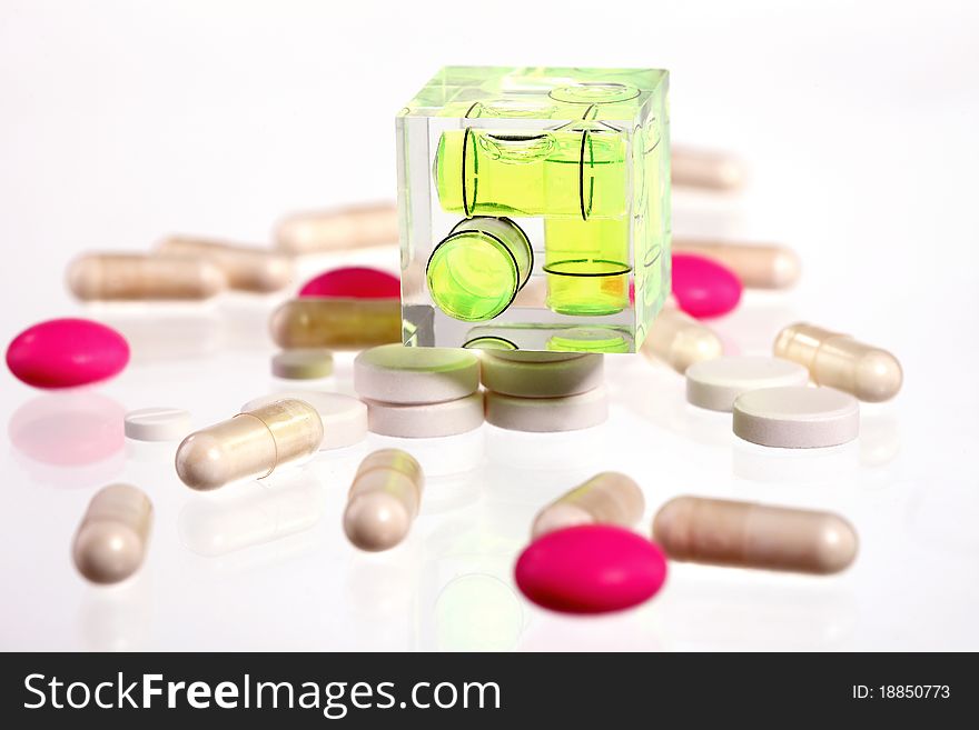 Pink and white pills on a white background with a small level on top of them. Pink and white pills on a white background with a small level on top of them