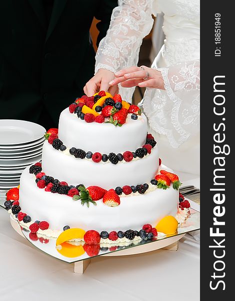 Cutting fresh wedding fruitcake with strawberries, raspberries, blackberries, peaches and blueberries