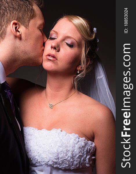 Groom kissing the bride against dark background