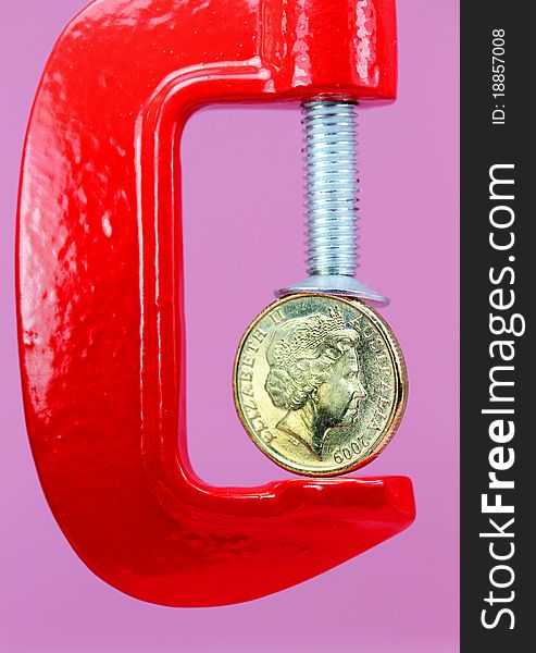 A gold coin held in a red clamp with a light pastel green background, indicating the pressure is on currency during these uncertain times. A gold coin held in a red clamp with a light pastel green background, indicating the pressure is on currency during these uncertain times.