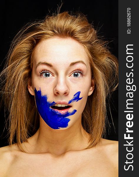 Beautiful young female is shocked. She is on black background with blue gouache color on her face and naked shoulders. Beautiful young female is shocked. She is on black background with blue gouache color on her face and naked shoulders.