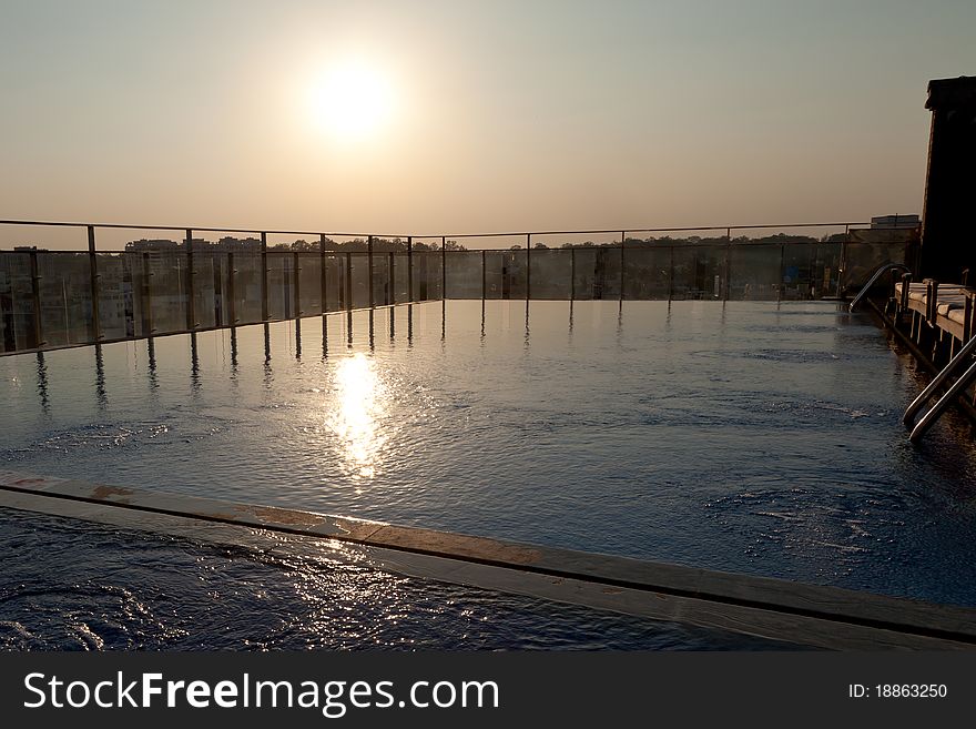 A hazy sun sets over an empty swimming pool on the roof of a city hotel. A hazy sun sets over an empty swimming pool on the roof of a city hotel.