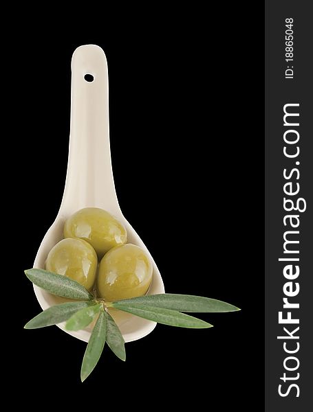 Olives in a spoon with leaves on a black background