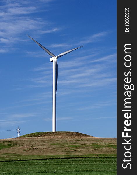 Photograph of a wind turbine against a bright blue sky with wispy clouds. Photograph of a wind turbine against a bright blue sky with wispy clouds.