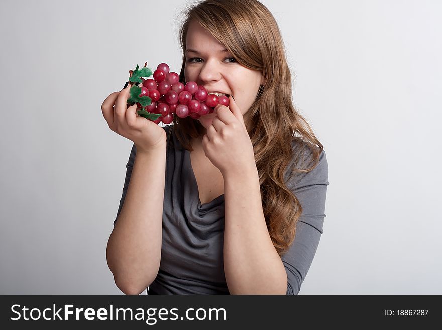 Girl on a light background is eating grapes. Girl on a light background is eating grapes