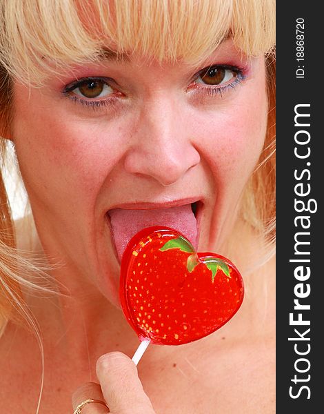 Blond woman licks red strawberry lollipop. Blond woman licks red strawberry lollipop