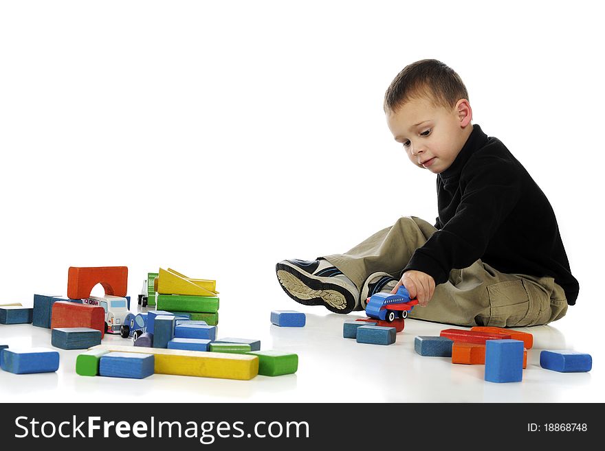 A preschool boy playing with colorful blocks and small wooden vehicles. Isolated on white. A preschool boy playing with colorful blocks and small wooden vehicles. Isolated on white.